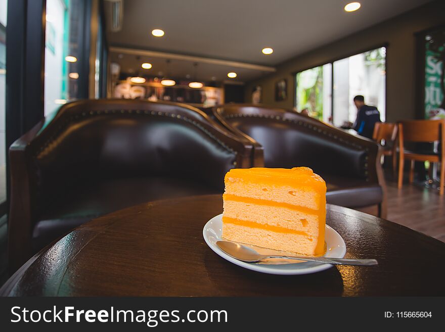 Orange cake on small white dish with spoon on table in coffee shop