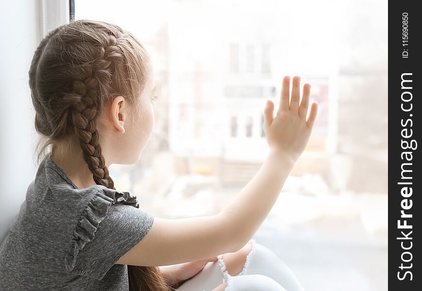 Lonely little girl near window indoors