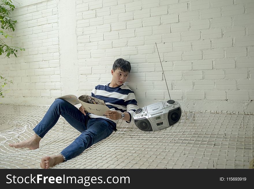 Boy Sitting Near Radio Holding White Catalog