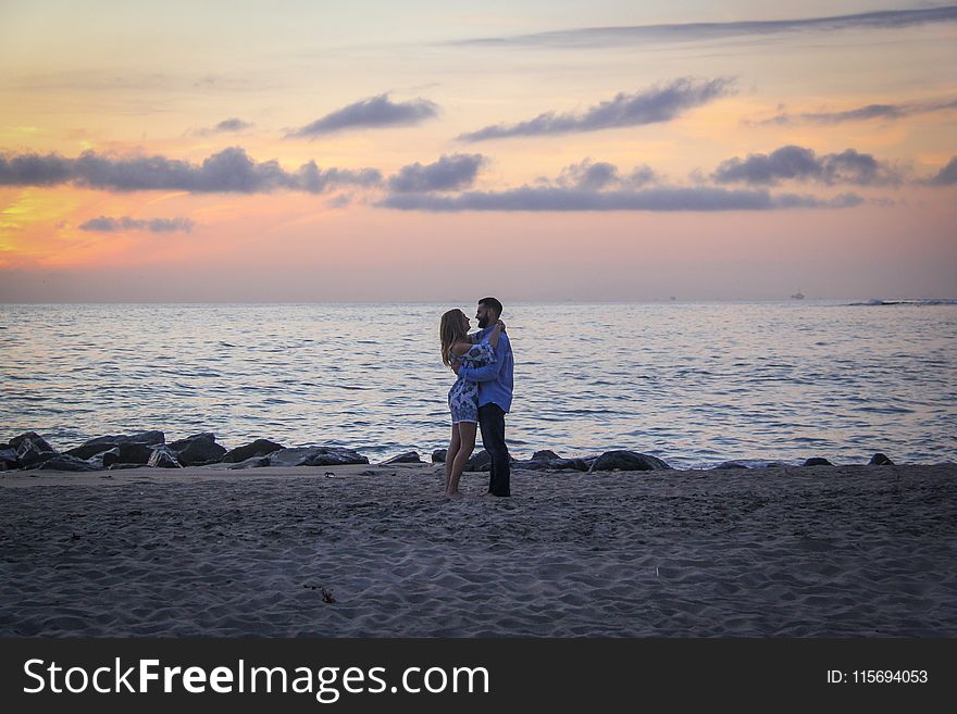 Couple Face To Face Stands On Seashore Near Calm Water During Golden Hour