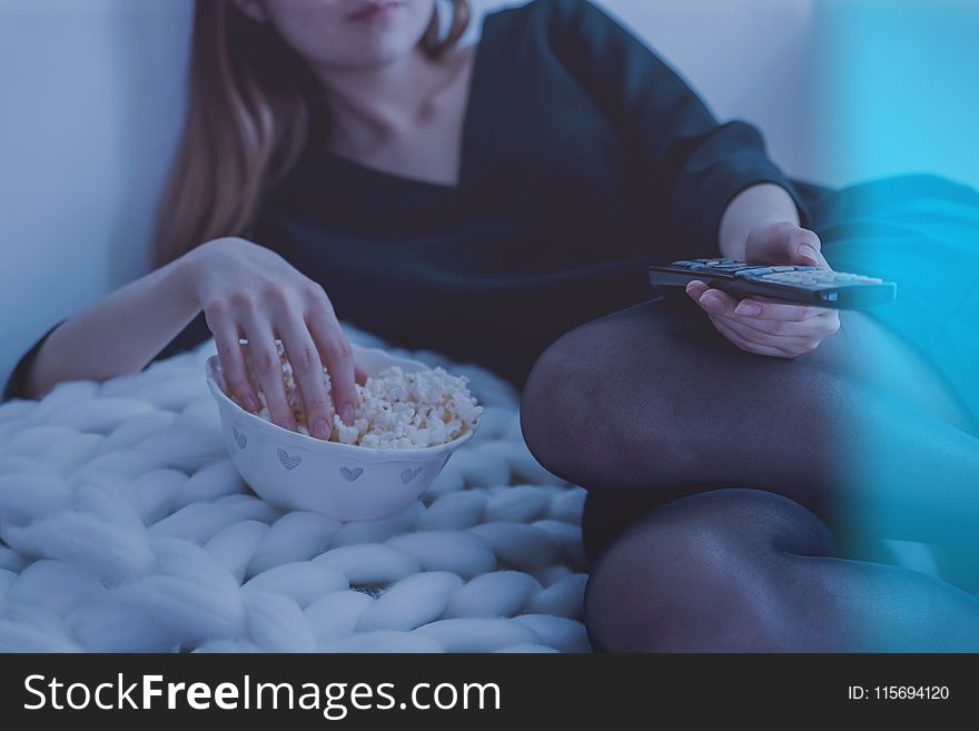 Woman in White Bed Holding Remote Control While Eating Popcorn