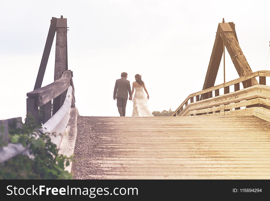 Man and Woman Holding Hands While Walking on Bridge