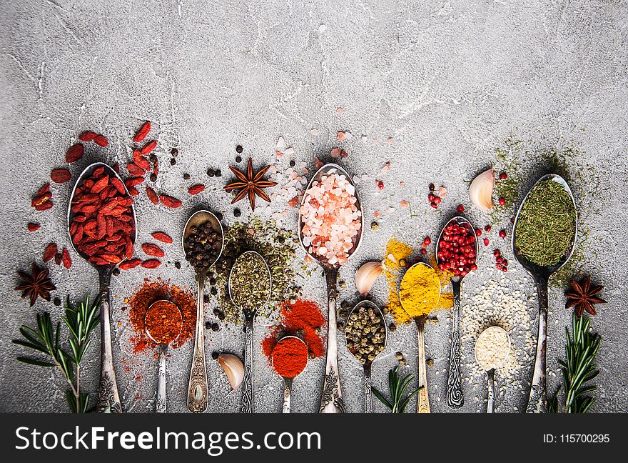 Different kind of spices in vintage spoons on a gray stone background