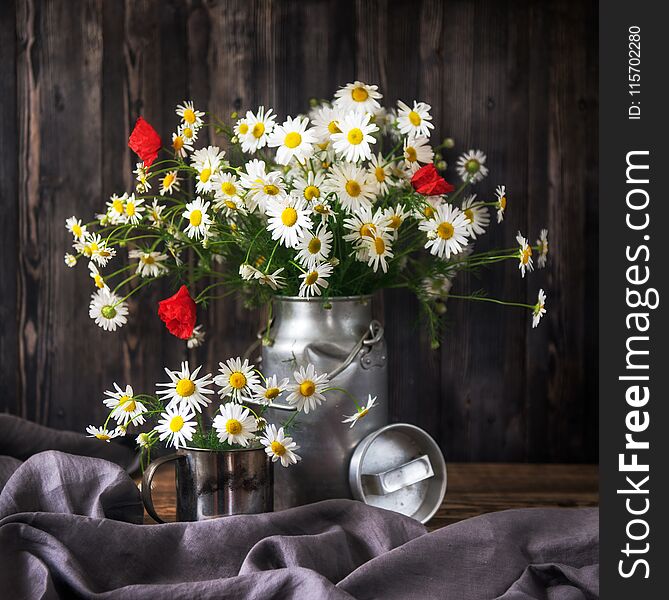 Rustic Still Life. Bouquet chamomile flowers and poppies in a metal can on a wooden background