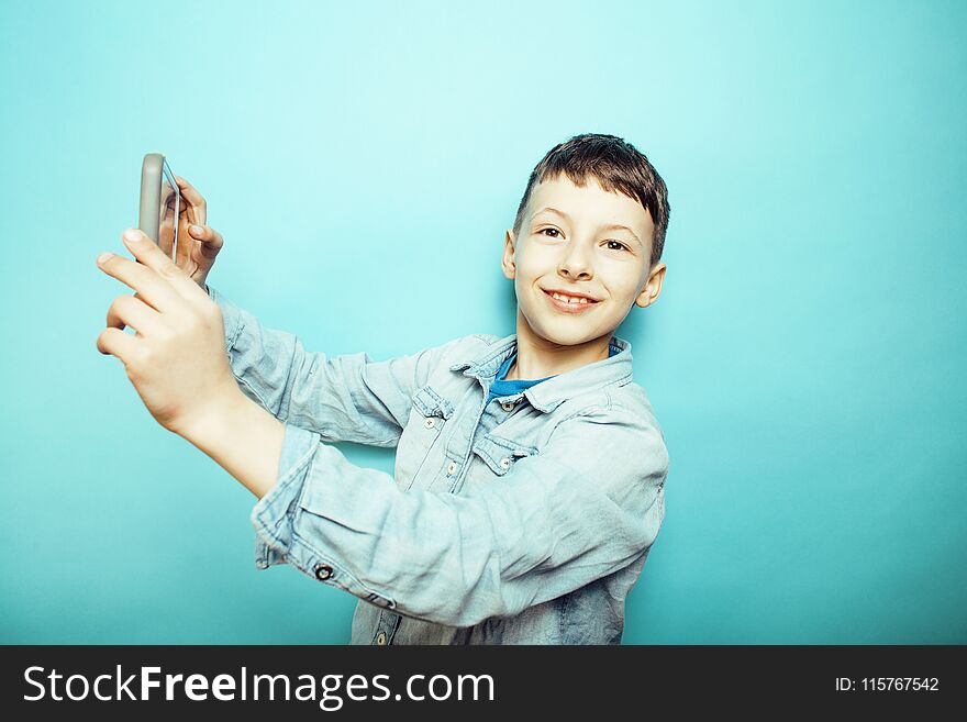 Little cute boy posing emotional on blue background with smartphone, lifestyle people concept close up