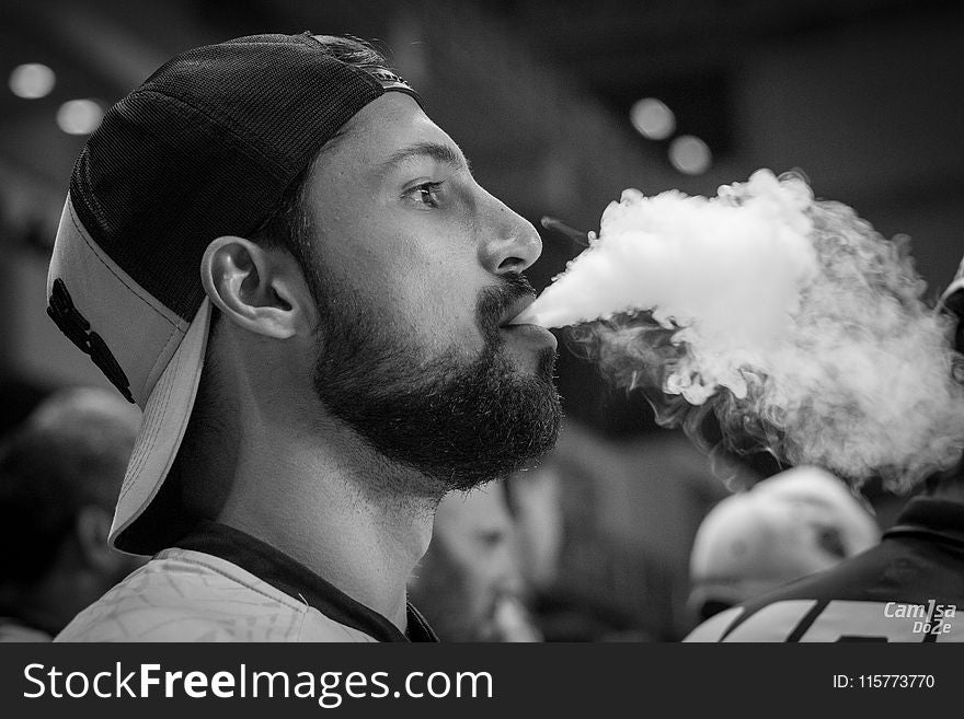 Grayscale Photography of Man Wearing Cap With Smoke on Mouth