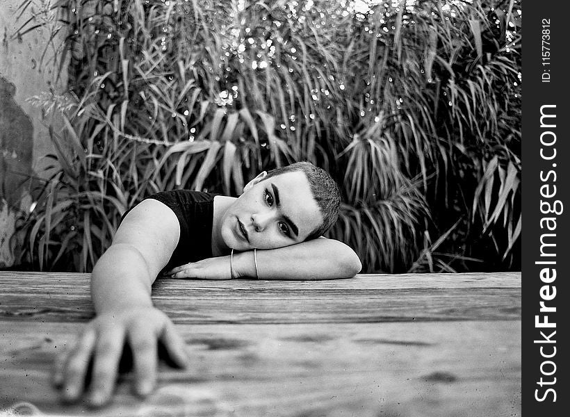 Grayscale Photo of a Person Leaning on Wooden Surface