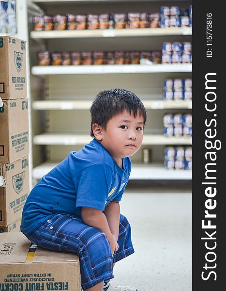Boy Wearing Blue Crew-neck T-shirt Sitting on Cardboard Box