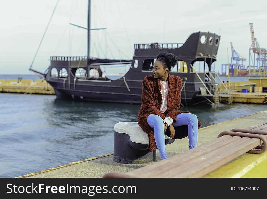 Woman in Red Cardigan Sitting on Black Metal Near Boats