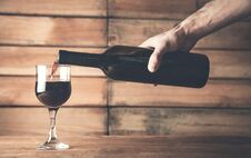 Hand Pouring Red Wine Into A Glass On A Wood Background Royalty Free Stock Images
