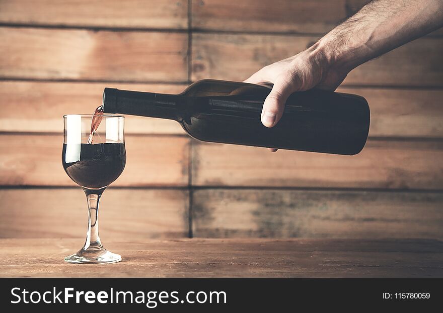 Hand Pouring Red Wine Into A Glass On A Wood Background