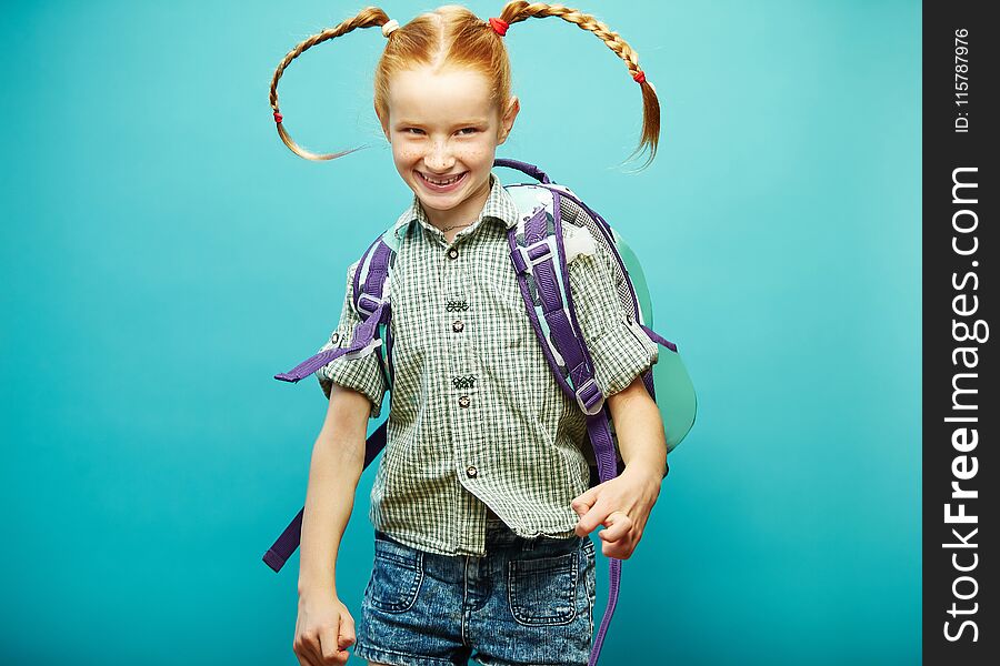 Cheerful Girl With Backpack On Her Shoulders Happily Jumping On Blue Background.