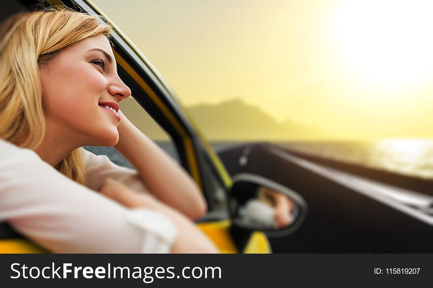 Travel or vacation. Beautiful blond girl in car on the road to the sea at sunset.
