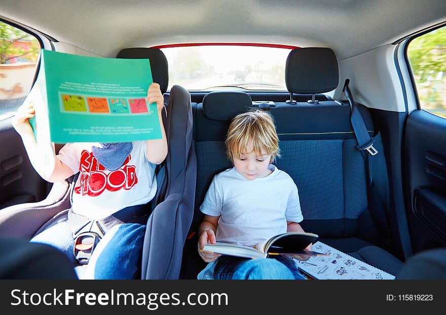 Two young kids sitting on back seat, reading book while traveling in the car