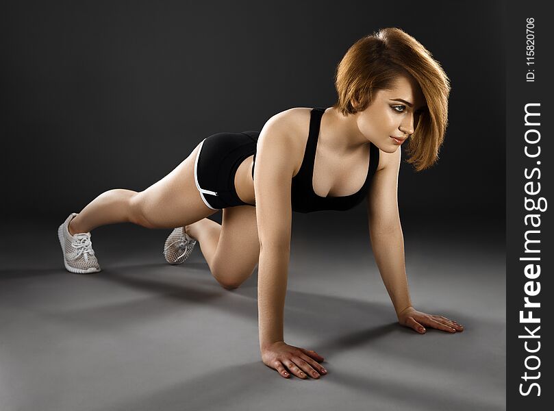 Beautiful young woman doing push-ups on a dark background