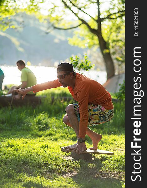 Man enthusiastically trains on the balance board on green meadow next to the river on sunny evening.