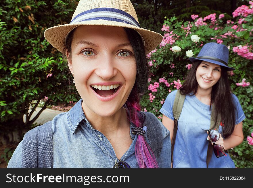 Two girls laugh, posing in the garden with blooming roses on a fisheye lens