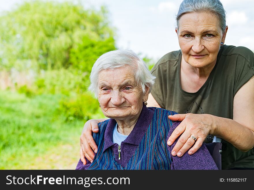 Senior woman with alzheimer disease sitting in wheelchair, posing with her daughter in the park. Senior woman with alzheimer disease sitting in wheelchair, posing with her daughter in the park