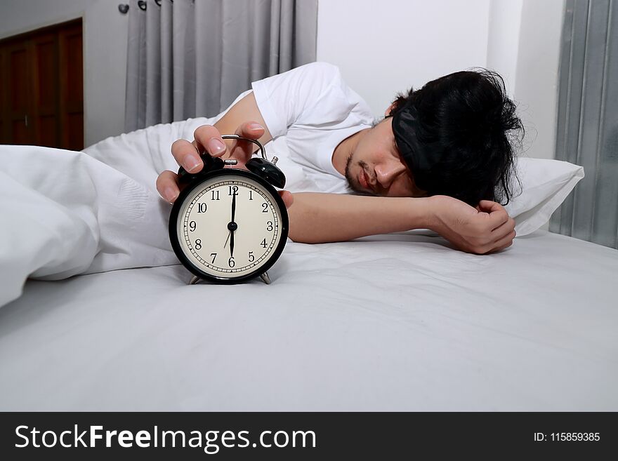 Young Asian man turn off alarm clock on the bed in morning .