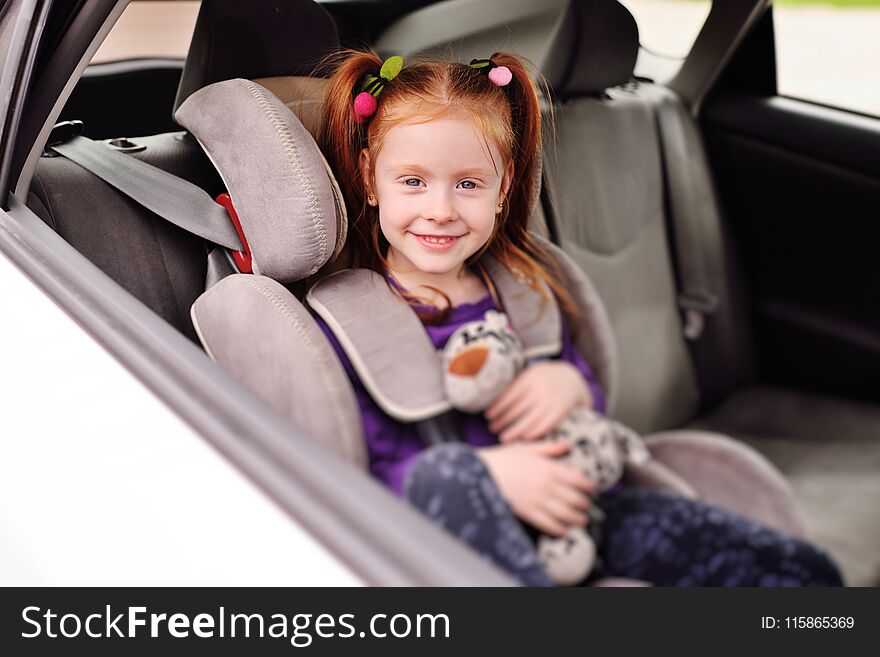 Baby little red-haired girl smiling while sitting in a child car seat.