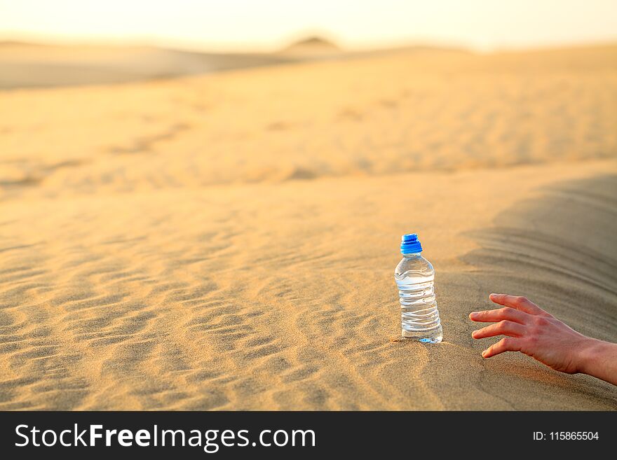 Hand try to catch the bottle of water on sand desert in hot temperature. Concept of to die of thirst.