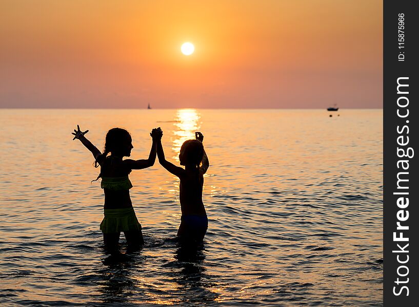 Silhouette of two young girl jumping in sea