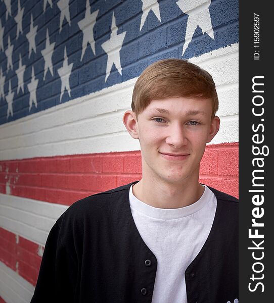 Caucasian teenage boy in front of a brick wall that has an American flag painted on it. Caucasian teenage boy in front of a brick wall that has an American flag painted on it.