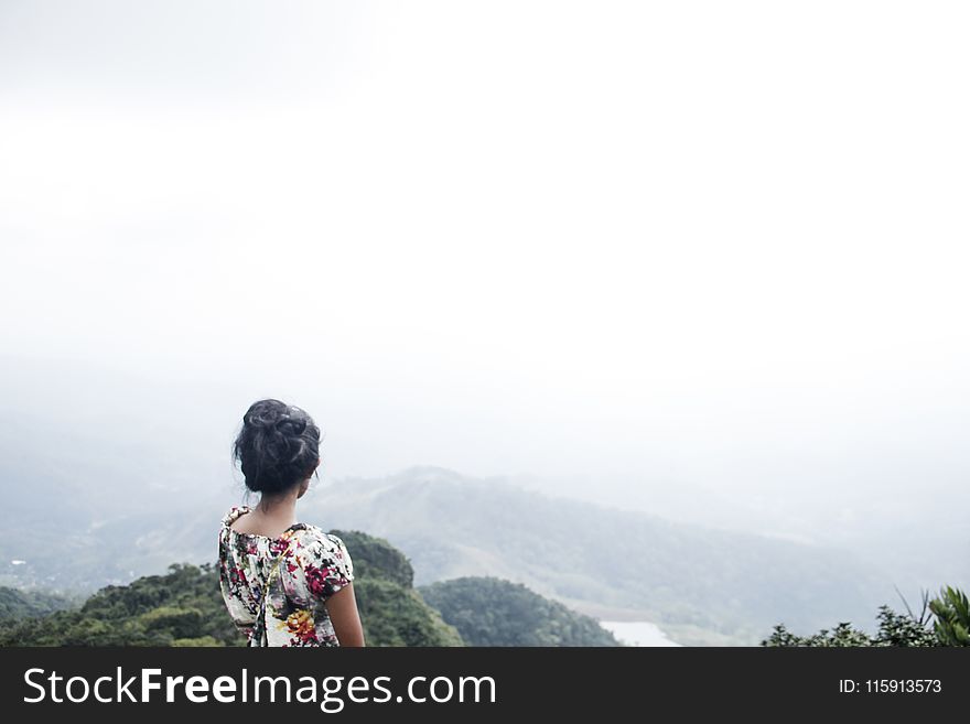 Woman Wearing Multicolored Floral Top Standing Near Mountain Under White Sky