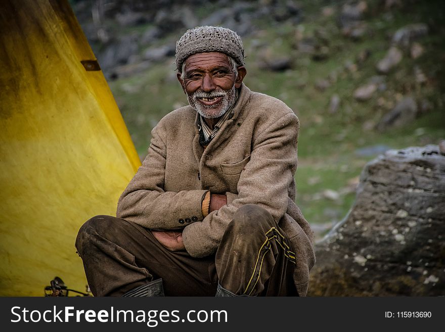 Smiling Man Wearing Gray Knit Cap Sitting Near Gray Rock