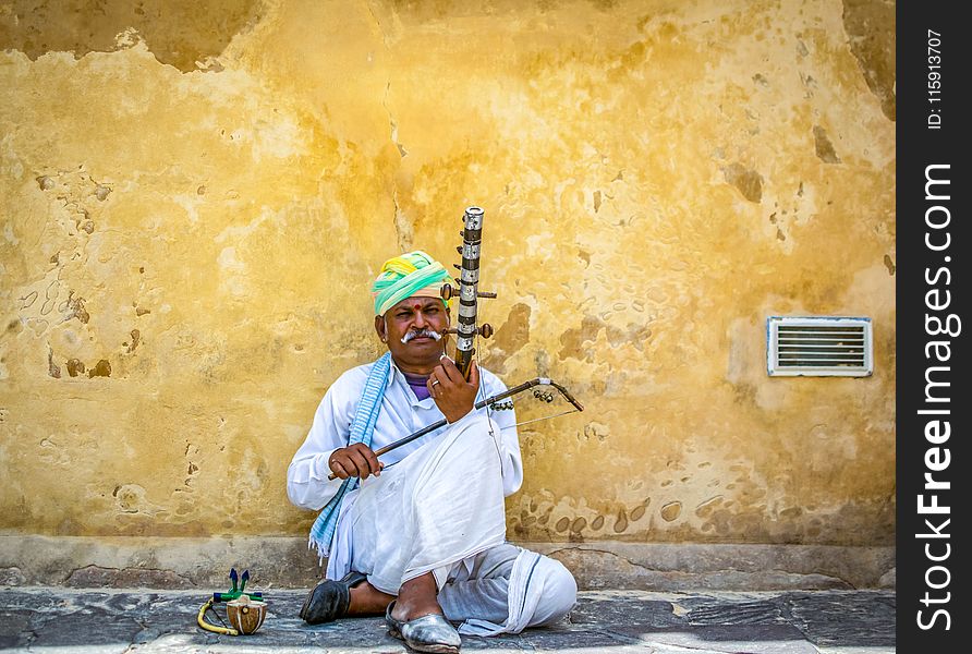 Man Holding String Instrument While Sitting on Concrete Pavement