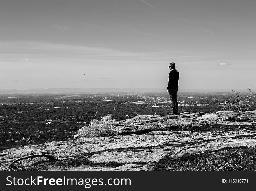 Greyscale Photography of Man Standing on Cliff in Front of Building