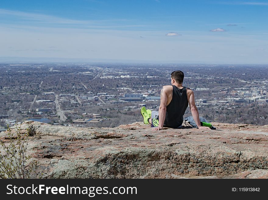 Man Wearing Black Tank Top Sitting Near Edge of Cliff