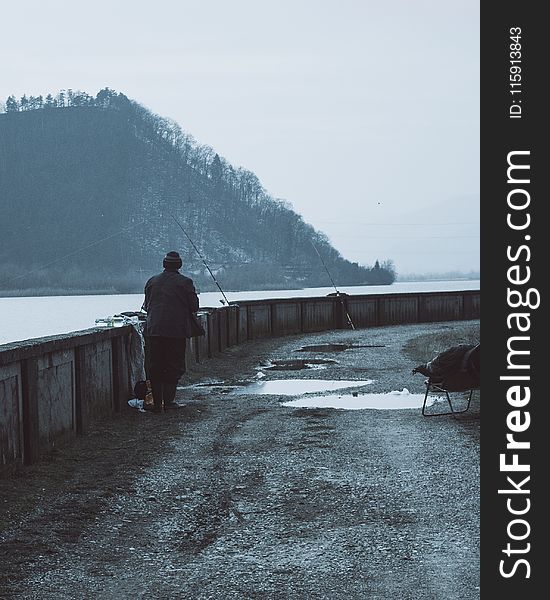 Man Wearing Brown Coat Near a Body of Water With Fishing Rods at Daytime