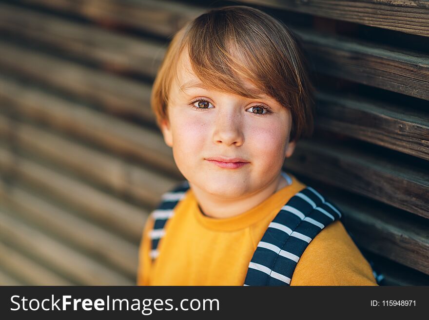 Outdoor portrait of cute kid boy wearing yellow sweatshirt and backpack. Back to school concept