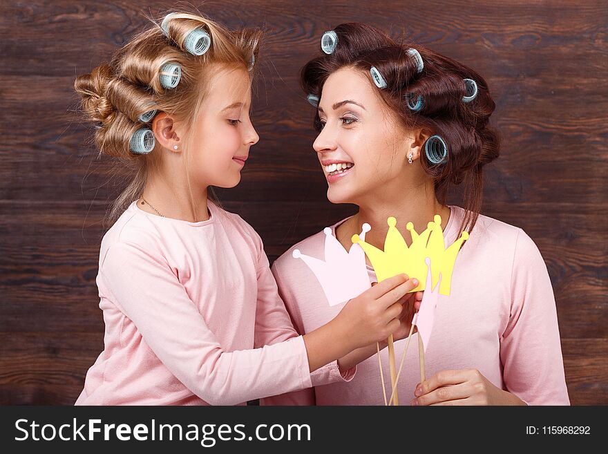Young mother and daughter with hair curlers having fun together and holding paper crown. Young mother and daughter with hair curlers having fun together and holding paper crown