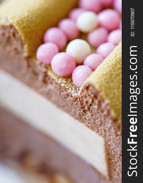 Luxurious round dessert with pink chocolate spheres. Yellow mousse birthday cake with multicoloured sweet sugar balls