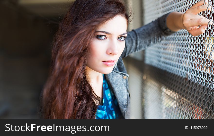 Woman Wearing Gray Denim Jacket Leaning on Gray Chain Link Fence at Daytime