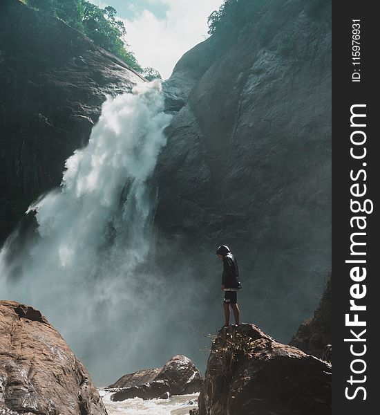 Man Standing On Brown Rock Cliff In Front Of Waterfalls Photography