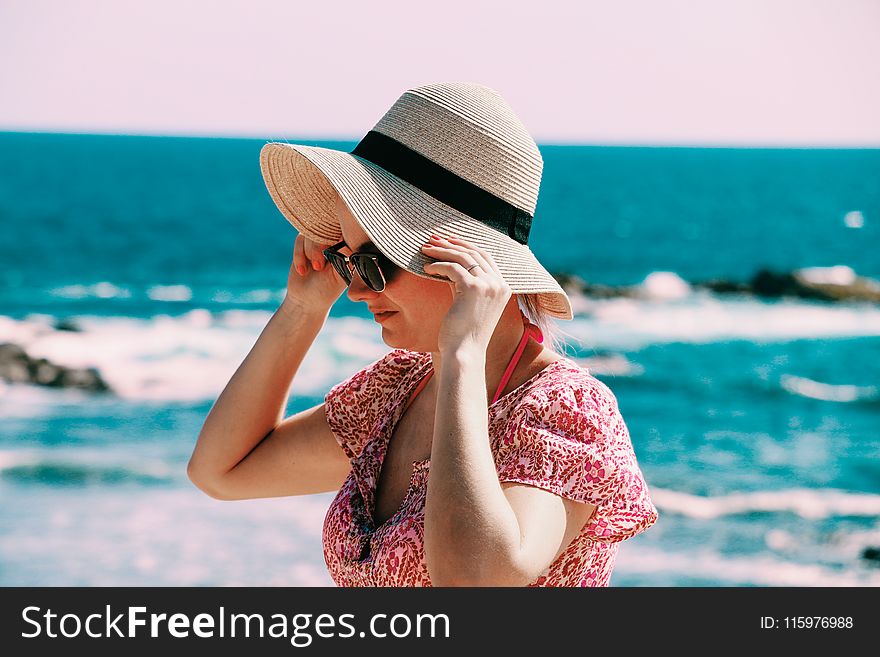 Selective Focus Photo of Woman Wears Beige Sun Hat Stand Behind Body of Water a Daytime
