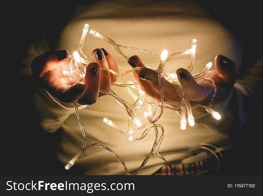 Closeup Photo Of Person Wearing White Long-sleeved Shirt Holding Turned On String Lights