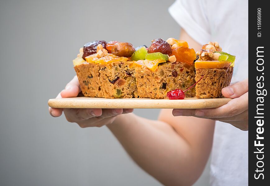 Female hand holding a loaf of fruit cake on wooden plate