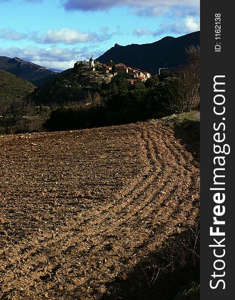 French village Cucugnan with a old mill on a hill and the ploughed ground on foreground.