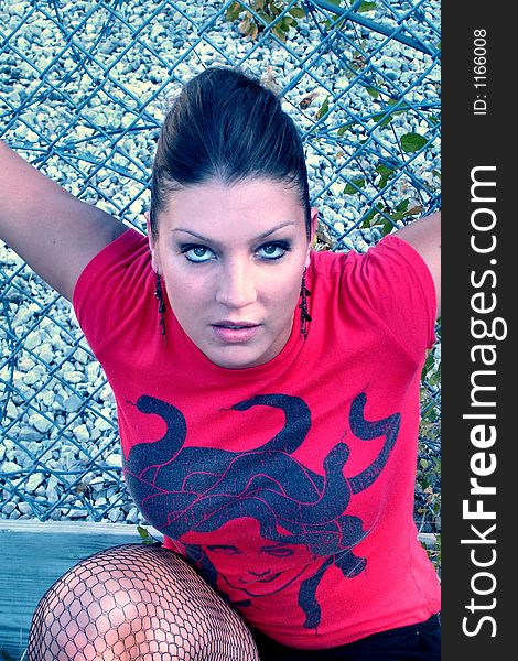 Punk woman kneeling in front of a chain link fence with a red shirt. Punk woman kneeling in front of a chain link fence with a red shirt.