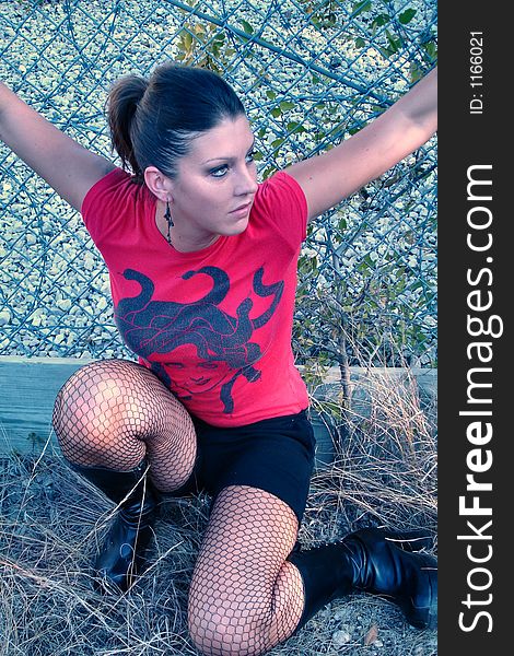 Punk woman kneeling in front of a chain link fence with black boots. Punk woman kneeling in front of a chain link fence with black boots.