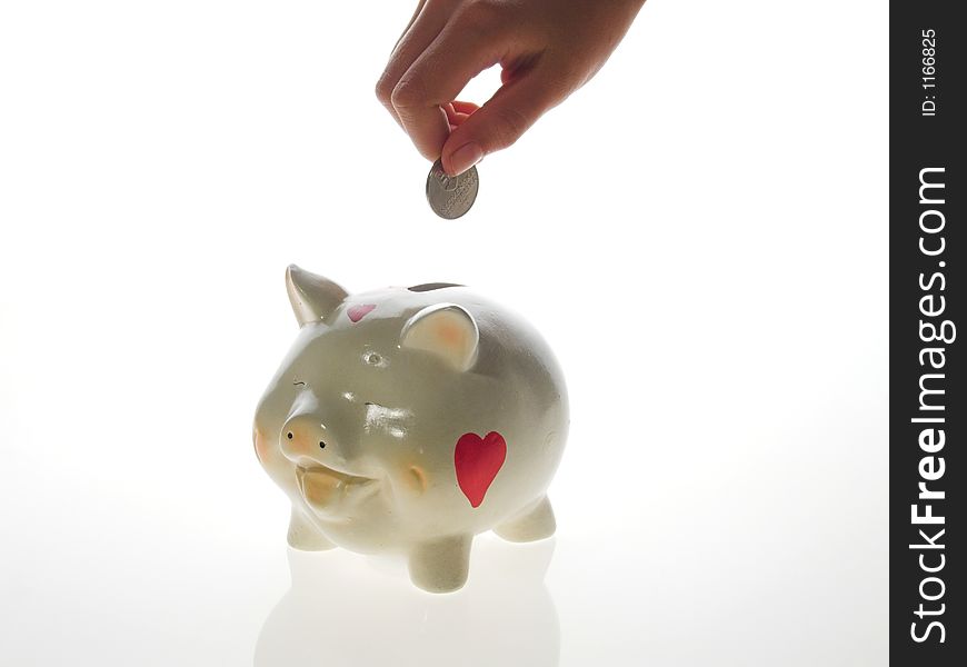 Piggy money-box on white background .a hand dropping a coin into a smiling piggy bank. Piggy money-box on white background .a hand dropping a coin into a smiling piggy bank