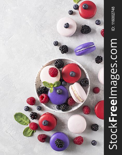 Raspberries, blackberries and blueberries macaroons over white texture, flat lay