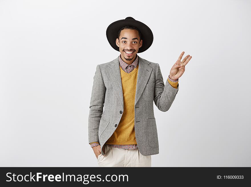 Showing Three Ways Or Choices. Studio Shot Of Pleased Successful African Boyfriend In Stylish Hat And Gray Jacket