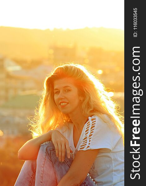 Smiling blonde girl in the sunlight, cityscape background