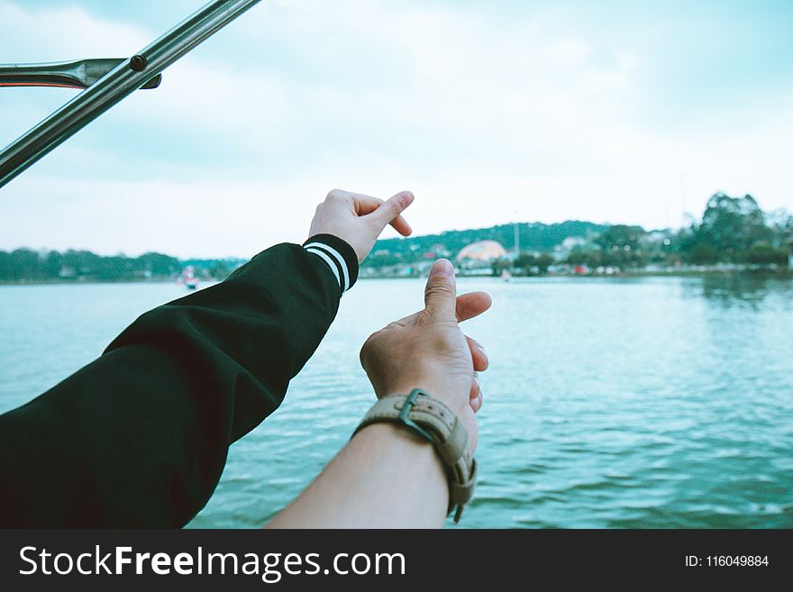 Two Person&#x27;s Left Hand Making Finger Heart Sign Near Body of Water