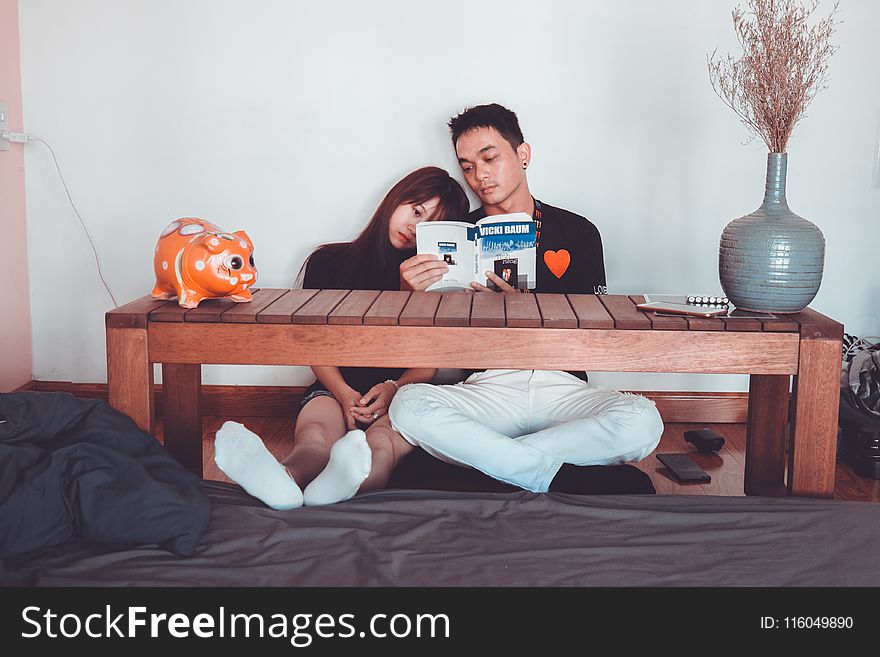 Couple Reading Book Sitting on Front of Rectangular Brown Wooden Coffee Table